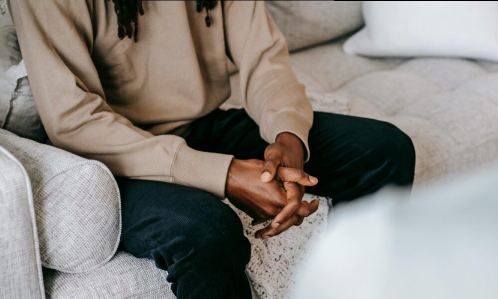 Man sits on counselling sofa with his hands linked together